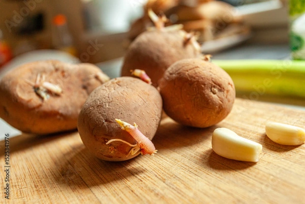 Fototapeta Sprouting potatoes and garlic on a board