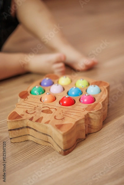 Obraz Boy playing with wooden fisherman toy sitting on the floor at home. Close-up. Educational activity for fine motor skills development.