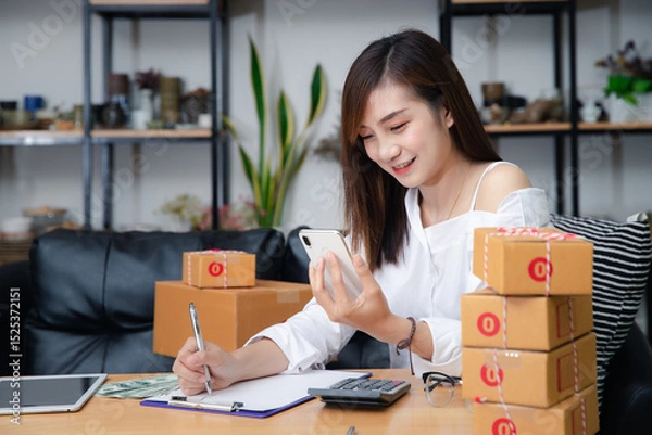 Obraz Woman are receiving orders via smartphone. Business woman owner holding parcel box for delivery shipping and using smartphone at home office. Business owner talking on mobile phone and taking order.