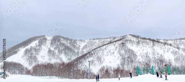 Fototapeta Snow mountains and hills covered with snow in winter under cloudy sky in Japan with unrecognized tourists