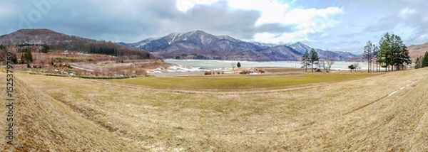 Fototapeta Panorama view of Lake Kanayama in Furano, in after winter season, no lavender field, no snow, under cloudy sky in rainy day, Hokkaido, Japan