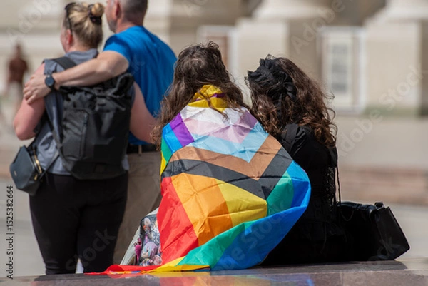 Fototapeta Couple of girls with rainbow coloured flag and heterosexual couple hugging during a LGBT+ pride parade