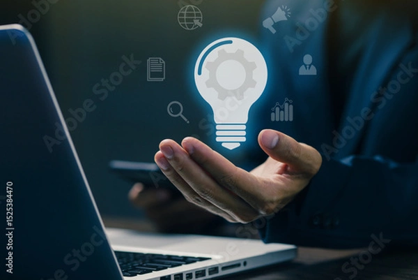 Fototapeta A businessman holding a glowing lightbulb with digital business icons, symbolizing innovation, creative ideas, business strategy, and technology-driven solutions.