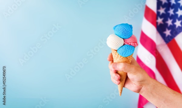 Obraz 4th of July Holiday background. Mans hand holds colorful ice cream cone with red, white and blue scoops patriotic colors on blue background and American flag. Happy Independence Day concept. Mock up.