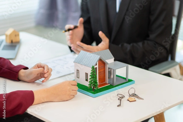 Obraz Inside a real estate office a real estate agent is using a house mockup to present the design and promotions that the client will receive when they sign sales contract. Real estate investment concept