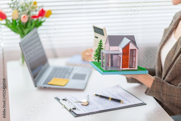 Obraz Inside a real estate office a real estate agent is using a house mockup to present the design and promotions that the client will receive when they sign sales contract. Real estate investment concept