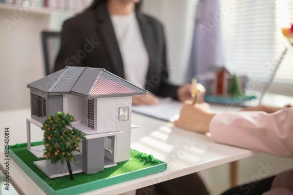 Obraz Inside a real estate office a real estate agent is using a house mockup to present the design and promotions that the client will receive when they sign sales contract. Real estate investment concept