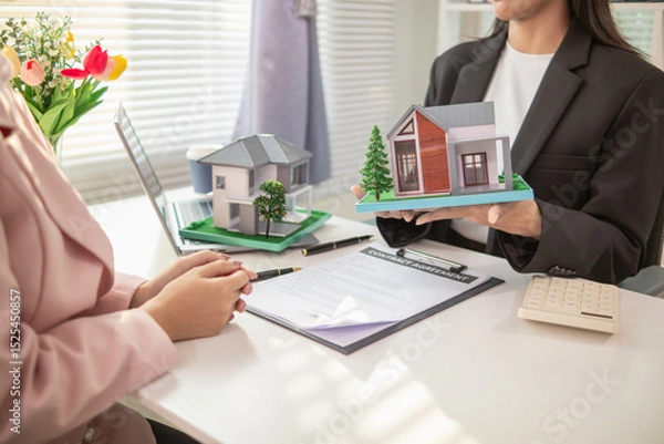 Obraz Inside a real estate office a real estate agent is using a house mockup to present the design and promotions that the client will receive when they sign sales contract. Real estate investment concept