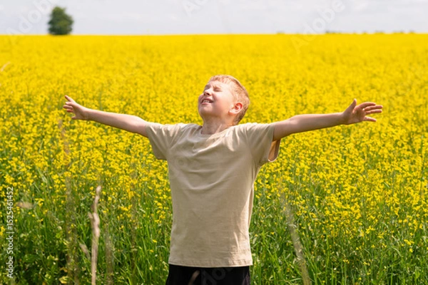 Fototapeta Happy blond boy with raised arms enjoying summer vacation in a yellow rapeseed field