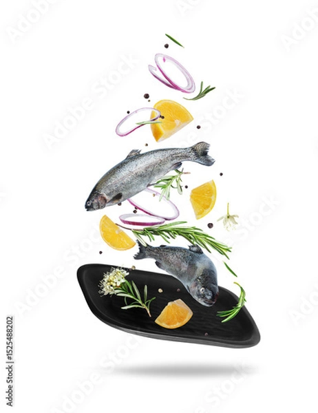 Fototapeta Sea trout with rosemary branches and lemon slices falling on a black clay plate, isolated on white background