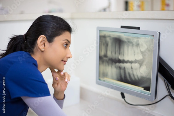 Obraz Closeup portrait of allied health dental professional in blue scrubs examining dental x-ray on computer screen, isolated dentist office