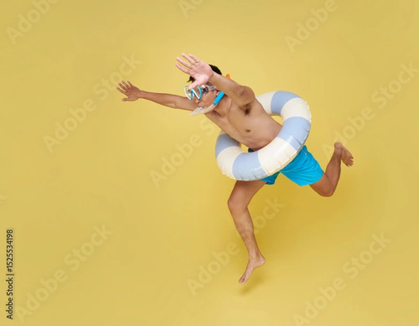 Fototapeta Full length cheerful young shirtless man in swim snorkel and inflatable ring jumping to dive having fun isolated on yellow copy space background.