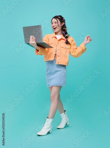 Fototapeta Full length Happy young beautiful Asian business woman using laptop While her walking isolated on blue background.
