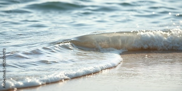 Fototapeta A gentle wave rolling onto the shore, creating a foamy edge where water meets the golden sand