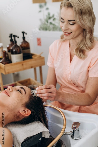 Fototapeta Scalp massage in spa salon using a handheld jade massager on long dark hair client