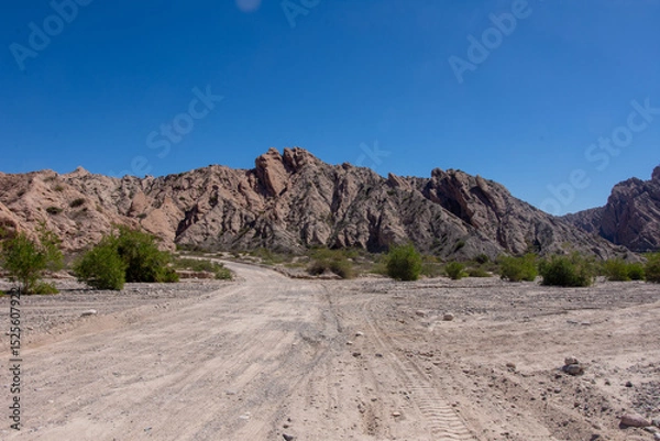 Fototapeta Dirt road in the desert named Quebrada de las Flechas with mountains of sedimentary rocks in Salta Province, Argentina