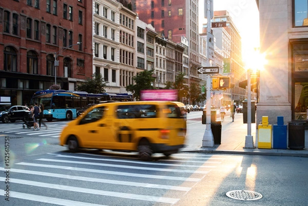 Fototapeta Busy intersection with people, taxis and buses on 5th Avenue and 23rd Street in New York City with sunlight shining in the background
