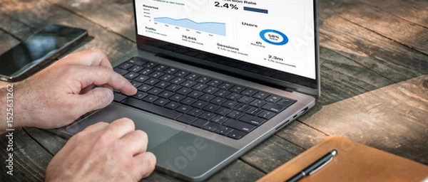 Fototapeta Entrepreneur using laptop to analyze traffic and user retention data. Modern business analytics workspace on wooden table with device and notebook