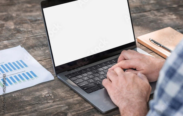 Fototapeta Male entrepreneur analyzing monthly conversion and click-through analytics on laptop at wooden table workspace. Remote work and data analysis concept