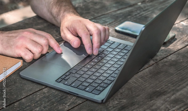 Fototapeta Closeup of male hands typing on laptop with blank screen on wooden table. Remote work concept