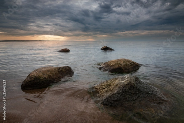 Obraz serene lake shore with boulders at sunset under dramatic cloudy sky