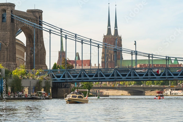 Fototapeta view across the Odra River toward Wroclaw's Grunwaldzki Bridge and Wroclaw Cathedral from the water. Boat cruise and vibrant riverside urban scenery on a warm day.