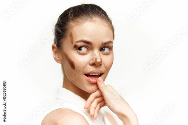 Fototapeta Young woman with playful expression showcasing beauty makeup techniques in a bright, minimalist setting demonstrating confidence and creativity.