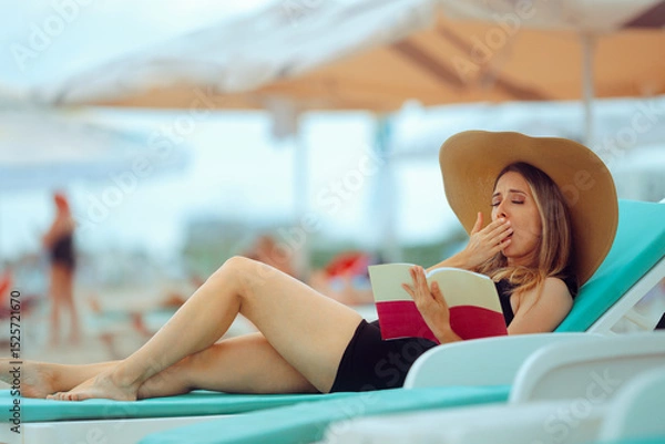 Fototapeta Woman Yawning from Boredom While Reading a Book on the Beach. Lonely lady at sea gets bored trying to finish a novel