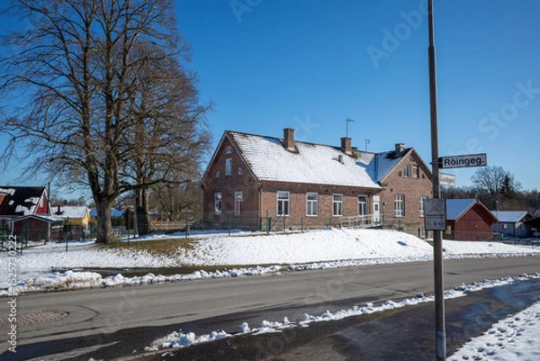 Obraz Old Roinge school building with snow-covered roof, a street sign, and winter landscape in Haessleholm, Sweden