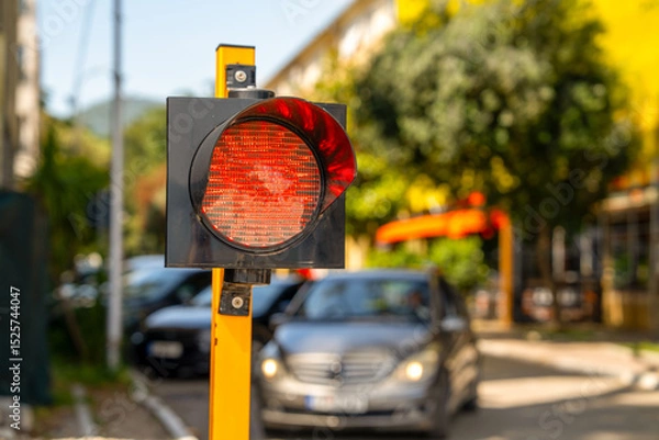 Fototapeta A red traffic signal, halting vehicles on a city street. cars wait at the intersection, emphasizing urban traffic flow and transportation themes.