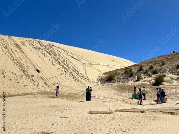 Fototapeta Tourists sand boarding down large sand dunes in Northland New Zealand. Giant Sand Dunes, are a collection of sand dunes located on the Northland Peninsula of New Zealand.