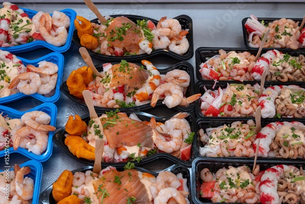 Obraz Sea street food for tourists on fish market on promenade in Oostende, Belgium, plastic box with variety of sea shells, shrimps, crab sticks, smoked fish