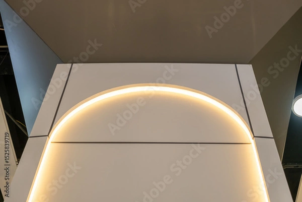 Fototapeta Architectural detail of a curved arch with integrated warm LED strip lighting. Modern interior design with minimalist lines and ceiling contrast. Abstract wall feature with soft illumination.