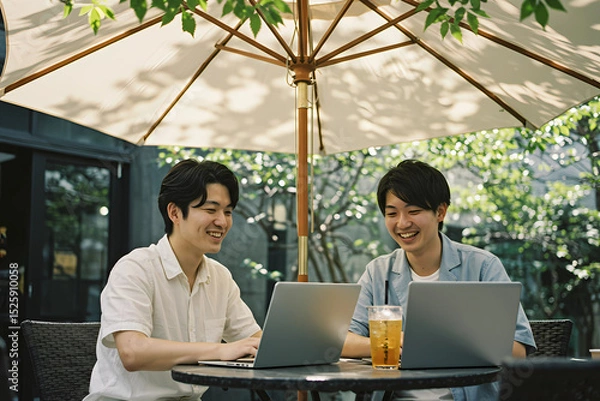 Fototapeta Portrait of two Young Asian enjoying drink together while working on laptop at outdoor cafe, representing remote work flexibility, entrepreneurship, and digital nomad lifestyle