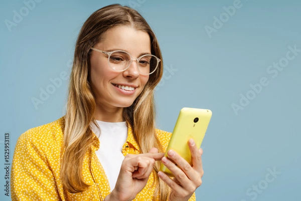 Obraz Happy young woman using a smartphone and smiling on a blue background