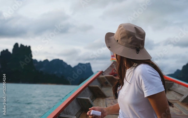 Fototapeta A woman sitting on a long tail boat and taking a photo while traveling on the river