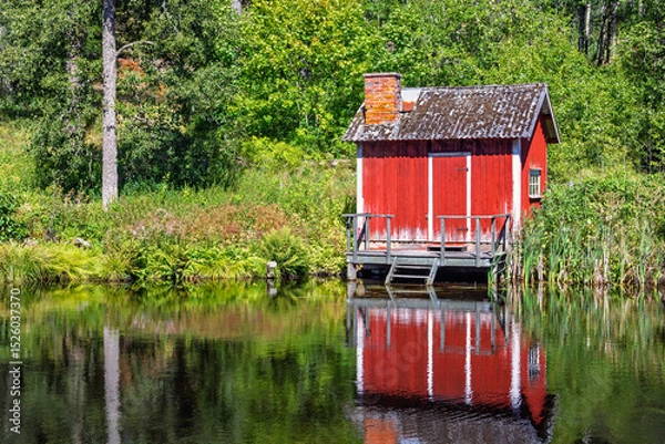 Obraz Idyllic Red wooden cottage on the lakeshore in the forest with reflections in the water