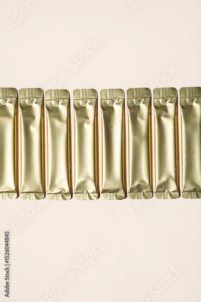 Fototapeta Row of Several Shiny Golden Sachets on a Light Background. Packaging for Powder Products.