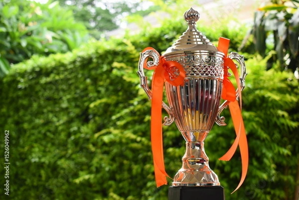 Fototapeta beautiful golden trophy with orange ribbon on green tree background
