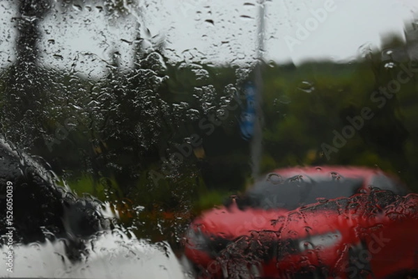 Fototapeta red car on parking in raining day, abstract blur background