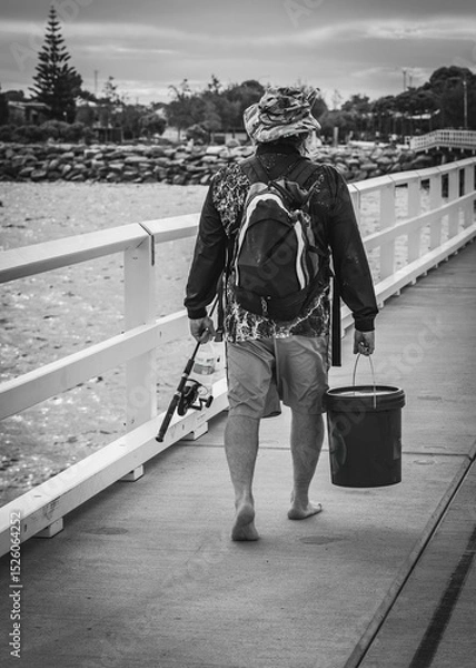 Obraz Esperance Western Australia - 12 29 2024: Black and white image of a man walking on a jetty with fishing gear.