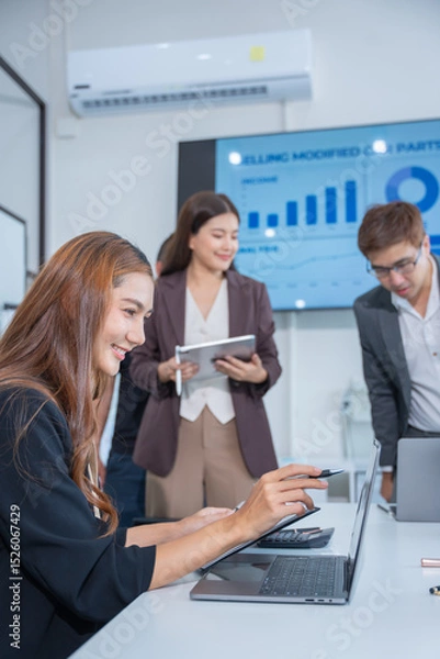 Obraz Group of business partners gathered around open laptop discussing company development strategies in modern office.