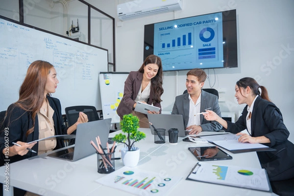 Obraz Group of business partners gathered around open laptop discussing company development strategies in modern office.