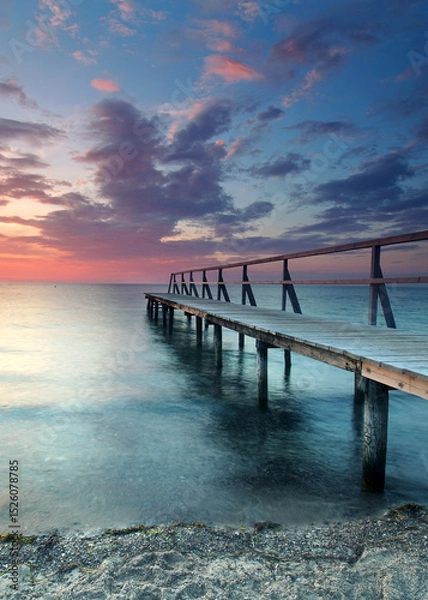 Fototapeta beautiful Vibrant Sunset Casting red Light on Weathered Wooden pier over the sea