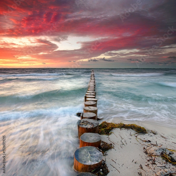 Fototapeta Raging Waves and red burning Skies: Weathered Wooden Groynes Amidst a Stormy Sea