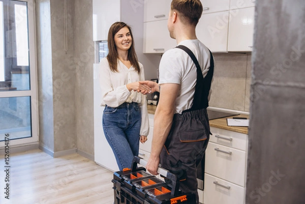 Obraz Plumber shaking hands with woman after finishing work in kitchen