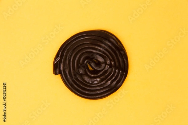 Obraz Black licorice wheel creates perfect spiral pattern on bright yellow background. Minimalist food photography showcasing confectionery design with bold color contrast.
