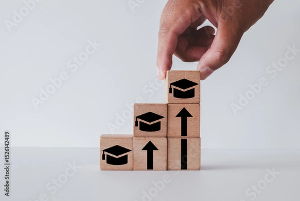 Obraz Hand stacking wooden blocks with graduation cap icons to form a staircase. Concept for higher education,step-by-step learning,professional development, continuous learning, skill improvement.