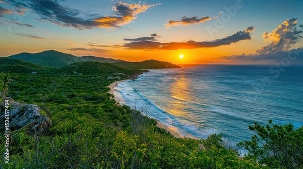 Fototapeta A breathtaking sunset over a lush green landscape with a calm ocean in the foreground and distant mountains in the background.