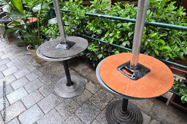 Fototapeta Urban Outdoor Cafe Setting with Empty Tables and Greenery on Stone Pavement